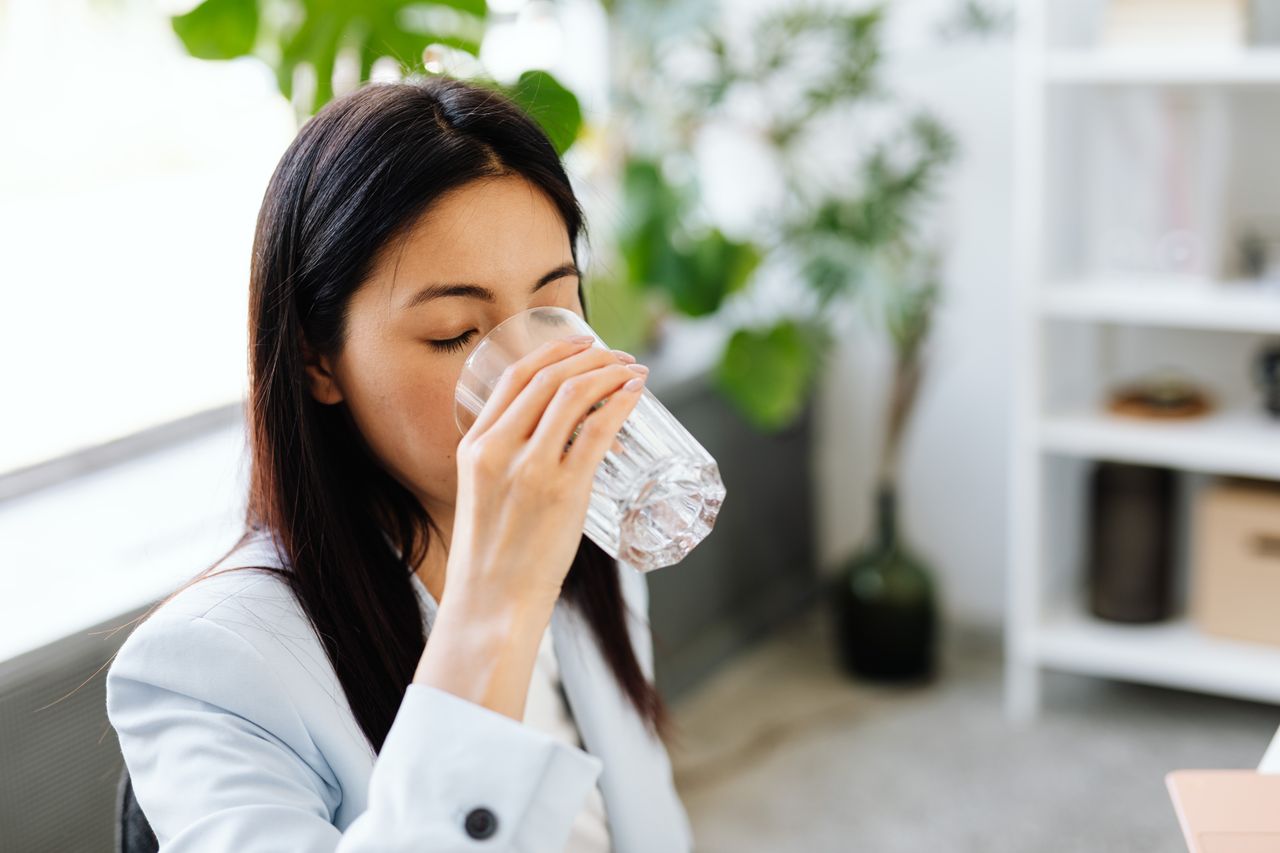 Adult woman sipping water from a glass in a modern office setting.