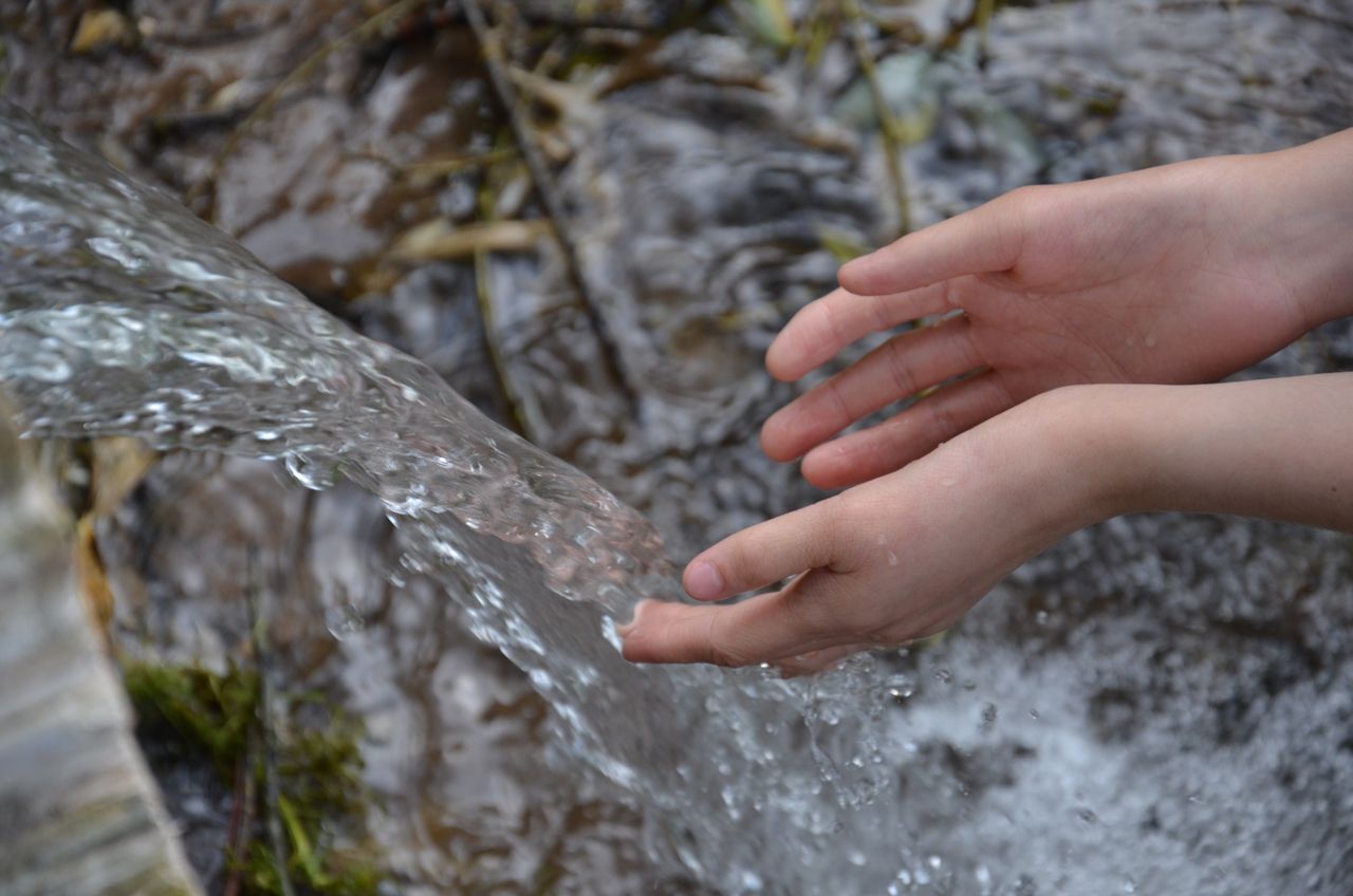 Close-up of hands catching fresh flowing water in a natural outdoor setting.